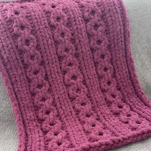 Könnte beinhalten: Eine weiche, rosafarbene Strickdecke mit einem Zopfmuster.