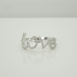 May include: A silver ring with the word "LOVE" spelled out in cursive, with small diamonds set into the letters.