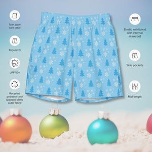 May include: Light blue swim trunks with a white snowflake and pine tree pattern. The trunks have an elastic waistband with an internal drawstring, side pockets, and a mid-length cut.