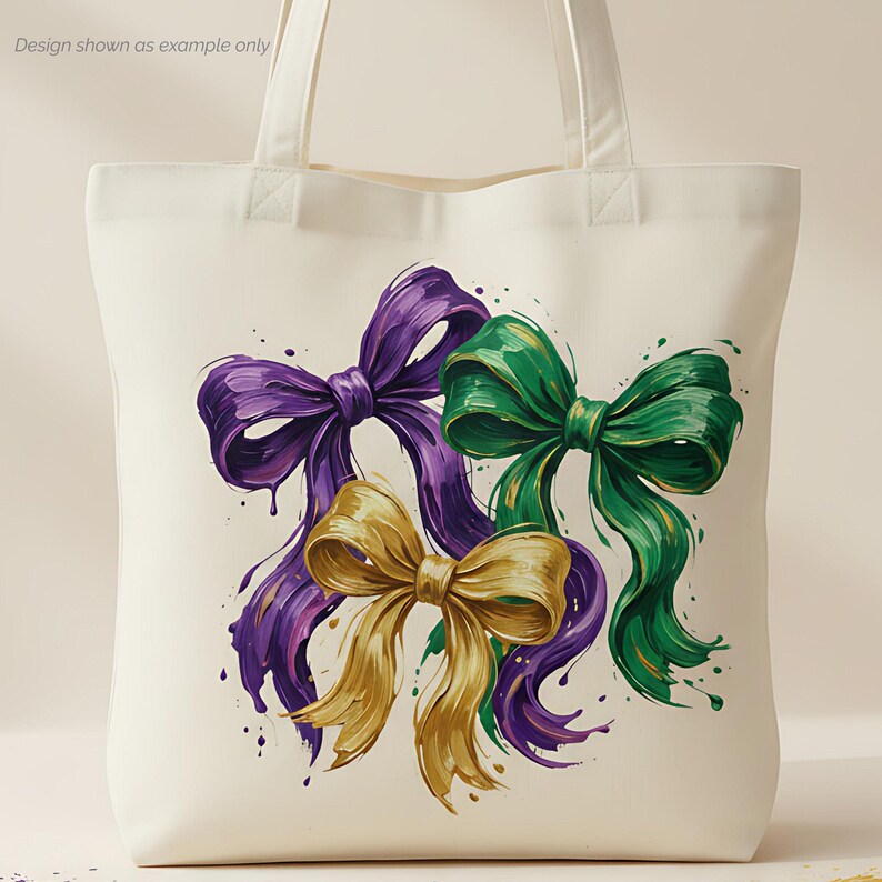 May include: Cream-colored tote bag featuring a watercolor design of three decorative bows. The bows are in shades of purple, gold, and green, with paint splatter accents. The design is a vibrant and artistic representation of festive bows.