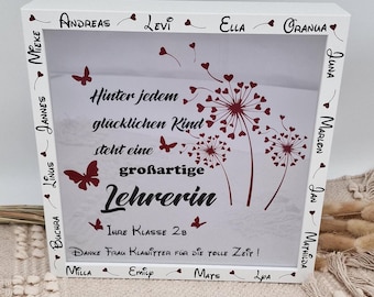 May include: White wooden frame with a white background and red text that reads "Hinter jedem glücklichen Kind steht eine großartige Lehrerin Ihre Klasse 2B Danke Frau Klawitter für die tolle Zeit!" with a dandelion design and red butterflies. The frame is surrounded by a border of names in red.