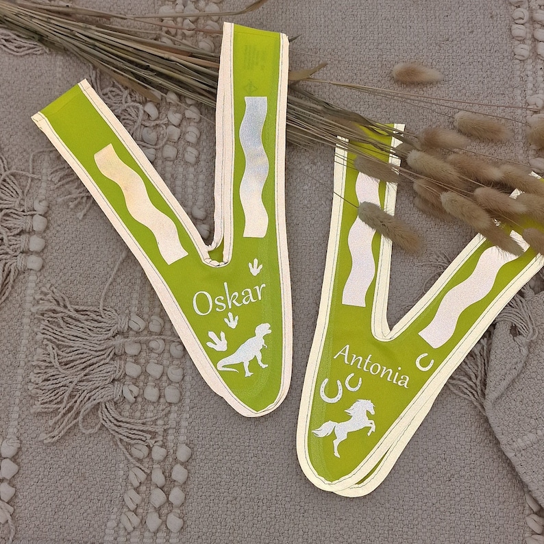 May include: Two green fabric sashes with white text and images. The sash on the left says "Oskar" and has a dinosaur silhouette. The sash on the right says "Antonia" and has a horse silhouette and a horseshoe.