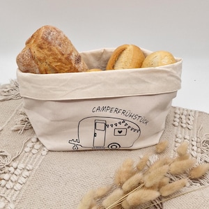 Könnte beinhalten: Ein weißer Stoff-Brotkorb mit einem schwarzen Wohnwagen-Design und dem Text "CAMPERFRÜHSTÜCK". Der Korb ist mit Brötchen gefüllt.