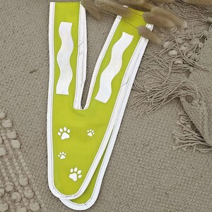May include: A lime green safety vest with white reflective strips and paw prints. The vest is designed for dogs.