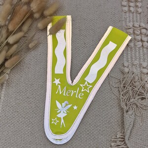 May include: A lime green safety vest with reflective white stripes and a silver star design. The vest has the name "Merle" and a fairy silhouette printed on it.