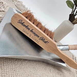 May include: A wooden dustpan and brush set. The brush has a light brown wooden handle with the text "Scherben bringen Gl&uuml;ck!" and the names "SARA & LUKAS" printed on it. The brush bristles are brown. The dustpan is silver.