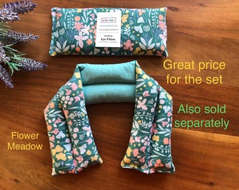 Könnte beinhalten: Zwei Augenpolster mit Blumenmuster "Flower Meadow". Die Kissen haben einen tealfarbenen Hintergrund mit rosa, gelben und weißen Blumen. Eines ist rechteckig, das andere ein U-förmiger Nackenwärmer. Für Entspannung.