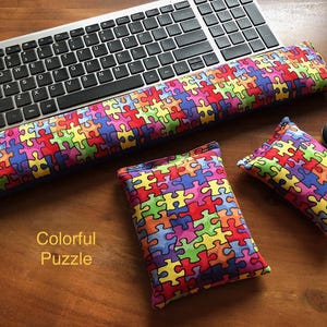 May include: A keyboard, mouse, and three colorful puzzle-patterned cushions rest on a wooden surface. The cushions are in various sizes, with a long one for the wrist and two smaller ones. The text "Colorful Puzzle" is visible.