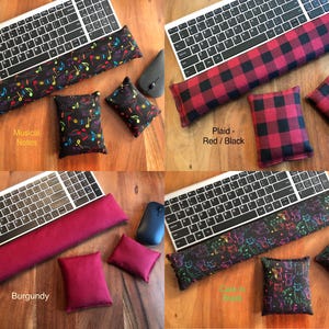 May include: Four keyboard wrist rests and matching small pillows in various designs. One features musical notes, another a red and black plaid pattern, a third is burgundy, and the last has a cat design. Each set includes a keyboard and mouse.