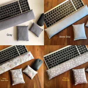 May include: A collection of keyboard wrist rests and matching mouse pads in various colors and patterns. The options include solid gray, stone gray, floral taupe gray, and a paper airplane design. Each set includes a keyboard rest, a mouse pad, and two small square pads.