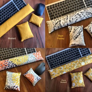 May include: Four keyboard wrist rests and matching small pillows in various colors and patterns. The options include mustard yellow, black paisley, coral bloom, and floral mustard. Each set includes a keyboard, mouse, wrist rest, and two pillows.