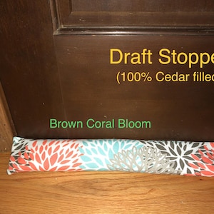 May include: A long, cylindrical draft stopper filled with 100% cedar, featuring a repeating floral pattern in coral, turquoise, and gray on a white background. The text Draft Stopper (100% Cedar filled) and Brown Coral Bloom is visible.