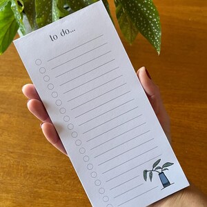May include: A white to-do list notepad with the words "to do..." at the top. The notepad has lined spaces for writing and a row of circles on the left. A small illustration of a plant in a blue vase is in the bottom right corner.