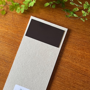 May include: A blank, rectangular, black magnet attached to a light brown cardboard backing.