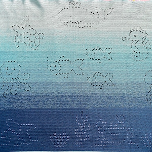 May include: A blue and white ombre crochet blanket with a variety of crocheted designs, including flowers, clouds, and a house.