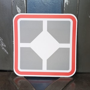 May include: Square sticker with a white center diamond and four gray corner squares. The design is outlined with a thin white border and a thicker red border. The sticker is on a dark surface.