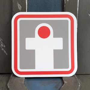 May include: A red and gray square sticker with a white symbol of a person with a red circle for a head. The symbol is inside a red border.