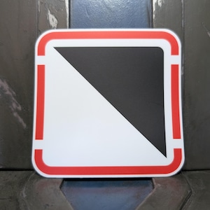 May include: A square sign with rounded corners, featuring a white background and a black triangle in the upper right corner. A red border frames the sign, with red vertical lines on the sides.