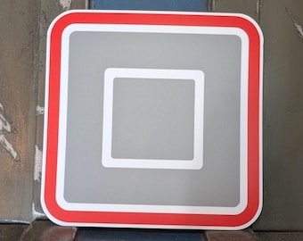 Pode incluir: Um autocolante quadrado com cantos arredondados. O autocolante tem um centro cinzento com um quadrado branco no meio. Uma borda branca envolve o centro cinzento e uma borda vermelha emoldura o autocolante.