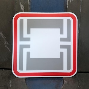May include: A square sticker with a white center, gray accents, and a red border. The design features a series of connected rectangles and lines, creating a modern, geometric pattern. The sticker is likely for decorative purposes.