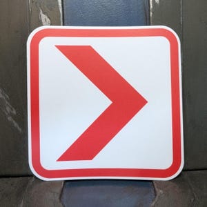 May include: A square sticker with a white background and a red arrow pointing to the right. The arrow is outlined with a red border, and the sticker has rounded corners.