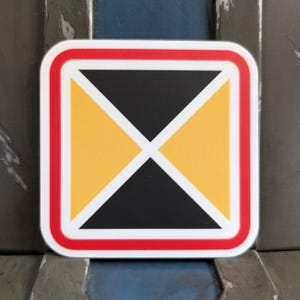 May include: Square sticker with a black and yellow geometric design. The design features a black triangle and a yellow triangle, separated by a white diagonal line. The sticker has a red border and a white border.