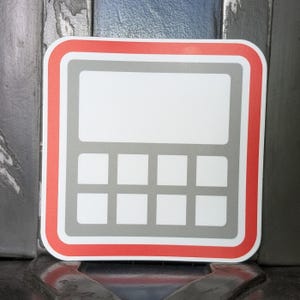 Puede incluir: Una pegatina con un diseño de calculadora. La pegatina tiene un fondo blanco con un contorno de calculadora gris y un borde rojo. La calculadora tiene un área de visualización en blanco y ocho botones cuadrados.