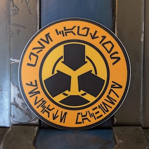 May include: A round yellow sticker with a black symbol in the centre. The symbol is a three-pointed star with arrows pointing inwards. The text around the symbol reads "ONI" in a stylised font.