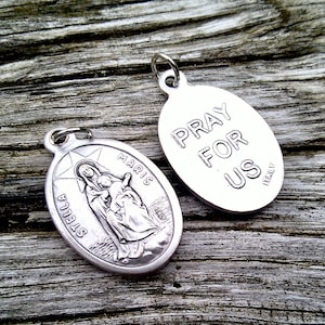 May include: Two silver oval pendants. One features a depiction of the Virgin Mary holding a baby Jesus. The other pendant reads "Pray for Us" in all caps.