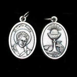 May include: Two silver oval pendants. One pendant features a portrait of St. Carlo Acutis with the text "St. Carlo Acutis". The other pendant shows a chalice, host, and grapes, with the text "Italy".