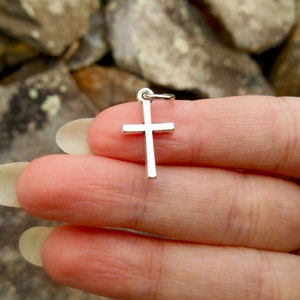 Puede incluir: Un colgante de cruz de plata. La cruz es simple y tiene un acabado liso y pulido.