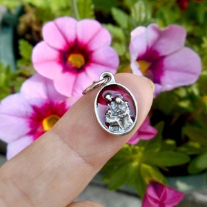 May include: A silver charm with a red enamel background depicting a family of three. The charm is oval shaped and has a loop at the top for attaching to a necklace or bracelet.