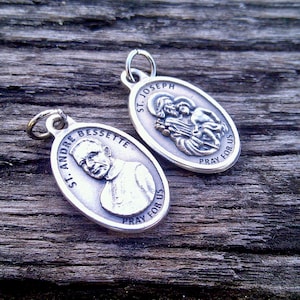 May include: Two silver oval-shaped religious medallions with images of saints. The top medallion features St. Joseph holding baby Jesus with the text "St. Joseph Pray for Us". The bottom medallion features St. Andre Bessette with the text "St. Andre Bessette Pray for Us".