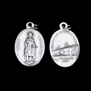 May include: Silver pendant with two sides. One side features a depiction of Saint Ferdinand, the other side shows the Mission San Fernando, California, founded in 1797.