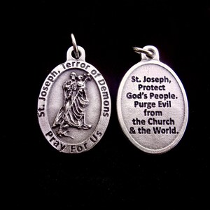 May include: Two oval silver-toned metal pendants. The left pendant features a relief of St. Joseph holding a child with the text St. Joseph, Terror of Demons, Pray For Us. The right pendant features the text St. Joseph, Protect God's People. Purge Evil from the Church & the World.