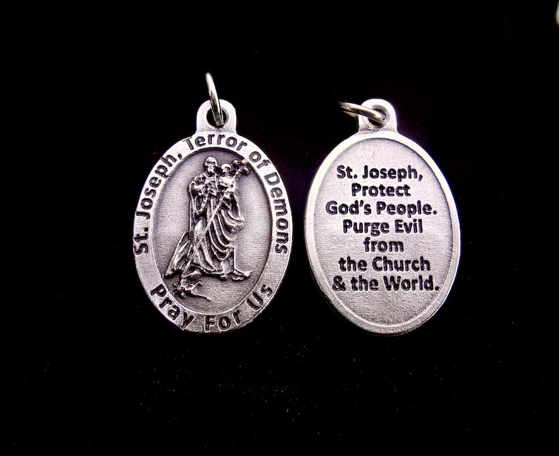 May include: Two oval silver-toned metal pendants. The left pendant features a relief of St. Joseph holding a child with the text St. Joseph, Terror of Demons, Pray For Us. The right pendant features the text St. Joseph, Protect God's People. Purge Evil from the Church & the World.