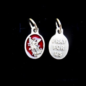 May include: Silver charm with a red enamel image of an angel on one side and the words "Pray For Us" on the other side.