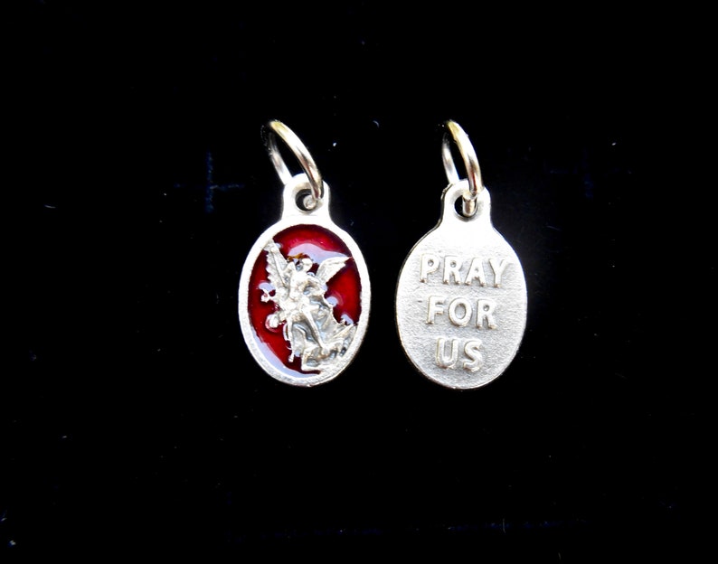 May include: Silver charm with a red enamel image of an angel on one side and the words "Pray For Us" on the other side.