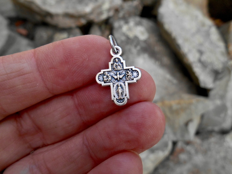 Puede incluir: Pendiente de plata en forma de cruz con cinco peque&ntilde;as figuras religiosas a cada lado. La cruz est&aacute; detallada con un acabado texturizado.