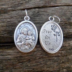 May include: Silver oval pendant with a depiction of Saint Joseph holding baby Jesus on one side and the words "Pray for Us Italy" on the other side.