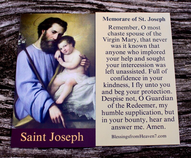 May include: A rectangular prayer card featuring a painting of Saint Joseph holding the infant Jesus on the left side, with the text Saint Joseph at the bottom. The right side contains the Memorare of St. Joseph prayer in black text on cream.