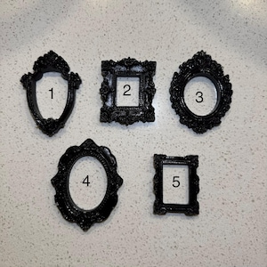 May include: Five black miniature picture frames with ornate, decorative edges. The frames are numbered one through five, featuring various shapes including shield, rectangular, and oval designs with intricate detailing on the borders.