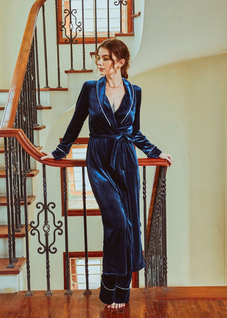 K&ouml;nnte beinhalten: Eine lange, dunkelblaue Samt-Robe mit wei&szlig;em Satinbesatz und einem passenden G&uuml;rtel. Die Robe wird von einer Person getragen, die auf einer Treppe steht.