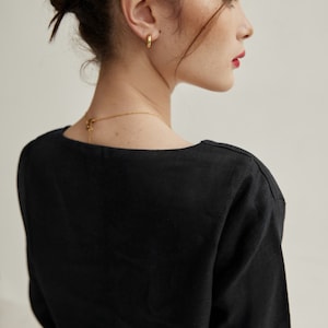 May include: A black, long-sleeved shirt with a square neckline. The shirt is made of a soft, lightweight fabric. The model is wearing gold hoop earrings.