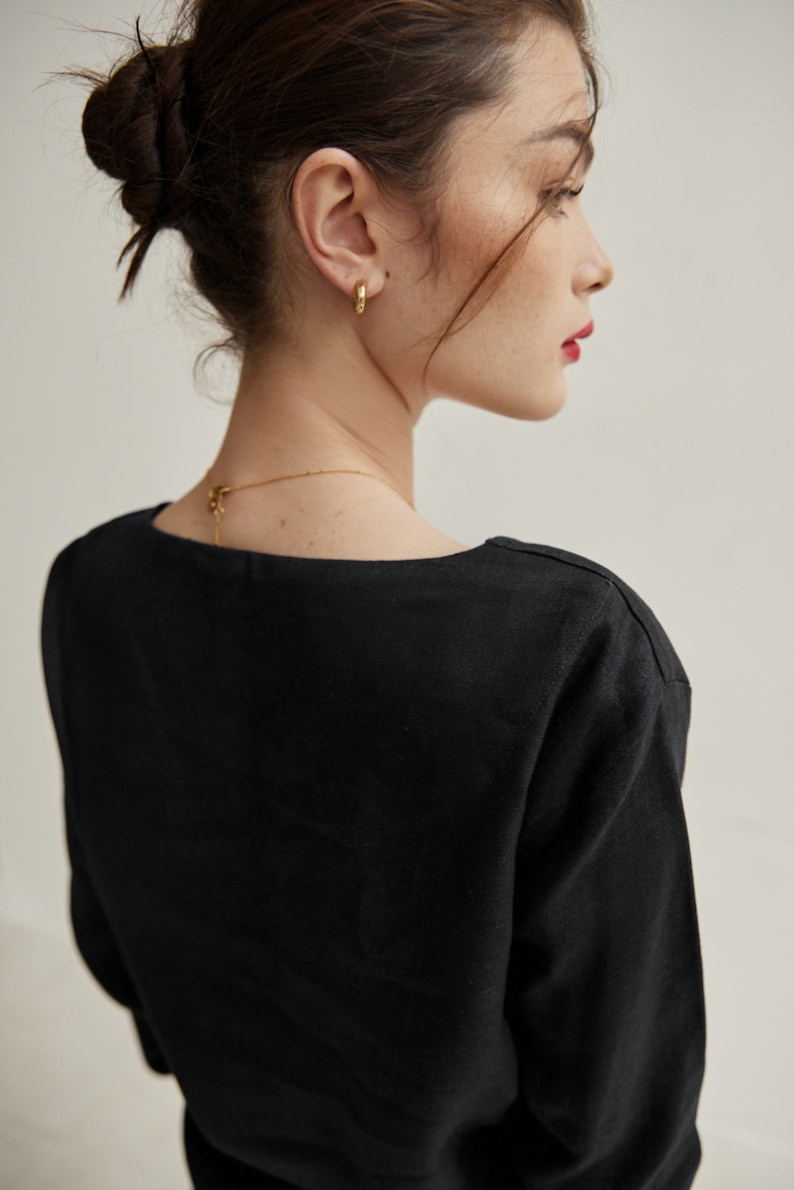 May include: A black, long-sleeved shirt with a square neckline. The shirt is made of a soft, lightweight fabric. The model is wearing gold hoop earrings.