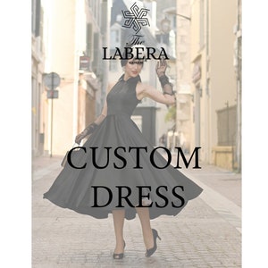 Op de afbeelding: Een vrouw in een zwarte, op maat gemaakte jurk met een volle rok, die op een straat met keien staat. De tekst "The Labera" en "Custom Dress" is zichtbaar in de afbeelding.
