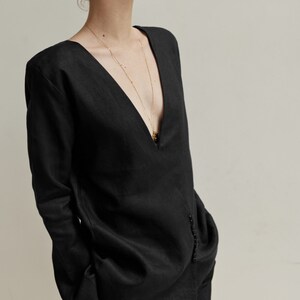 May include: A black linen shirt with a deep V-neckline and long sleeves. The shirt has a gold chain necklace with a pendant.