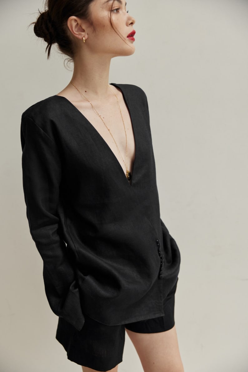 May include: A black linen shirt with a deep V-neckline and long sleeves. The shirt has a gold chain necklace with a pendant.
