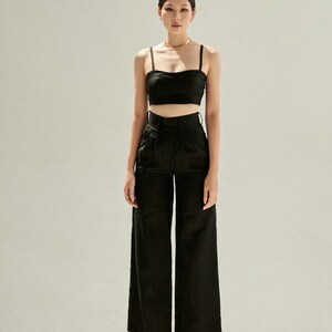 K&ouml;nnte beinhalten: Eine Frau tr&auml;gt ein schwarzes Crop-Top und eine weite Hose mit hoher Taille. Sie tr&auml;gt braune Sandalen mit Absatz.