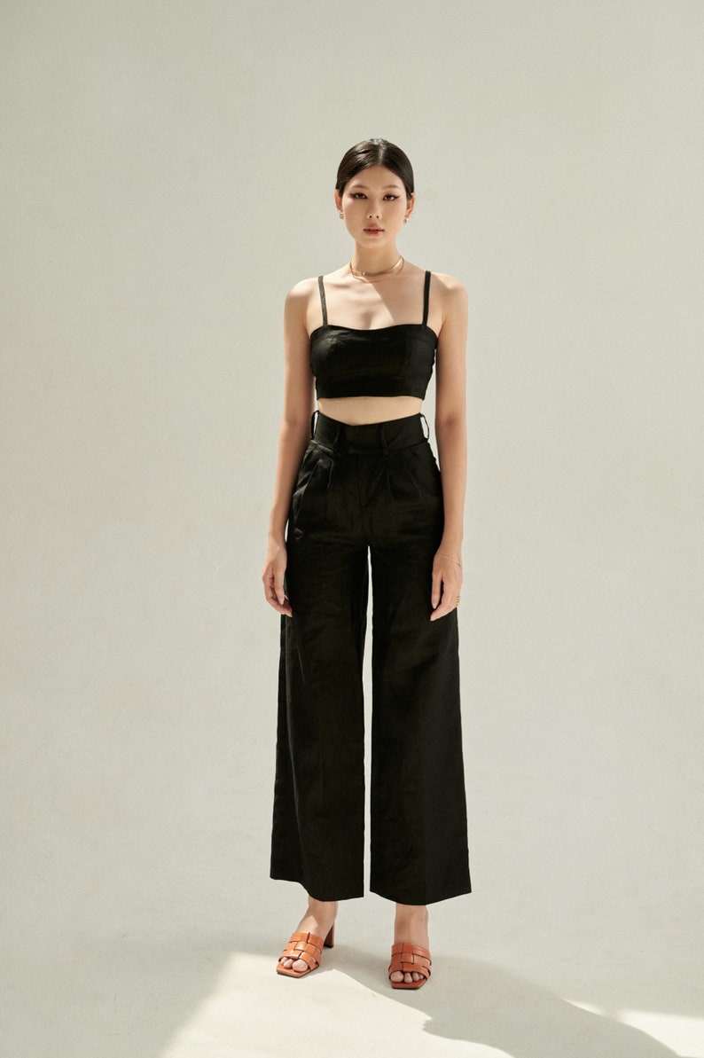 K&ouml;nnte beinhalten: Eine Frau tr&auml;gt ein schwarzes Crop-Top und eine weite Hose mit hoher Taille. Sie tr&auml;gt braune Sandalen mit Absatz.